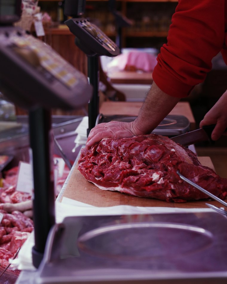 Le mani di un macellaio su un pezzo di carne, col coltello e la bilancia del banco