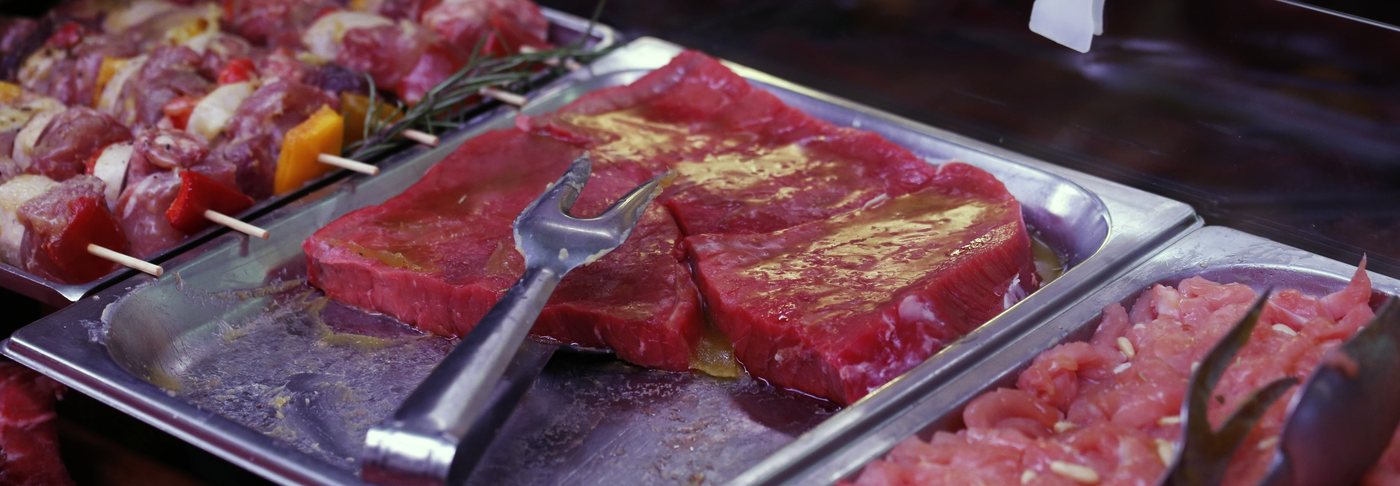 Un vassoio d’acciaio con una fetta grande di carne e gli spiedini, nel banco